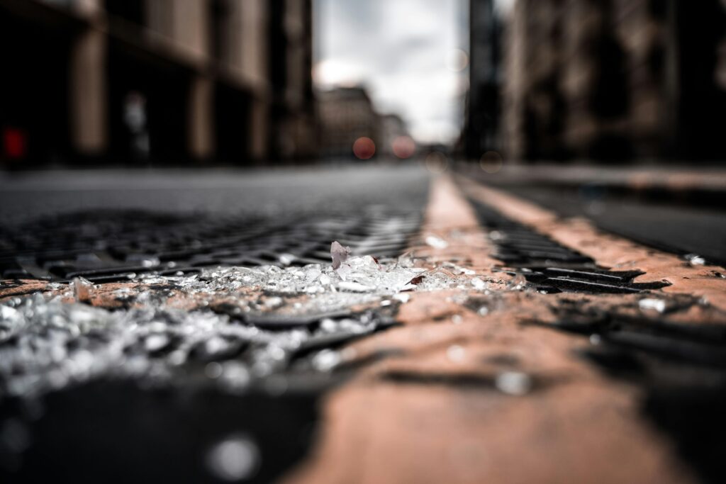 Close-up of broken glass pieces scattered on a city street with blurred buildings.